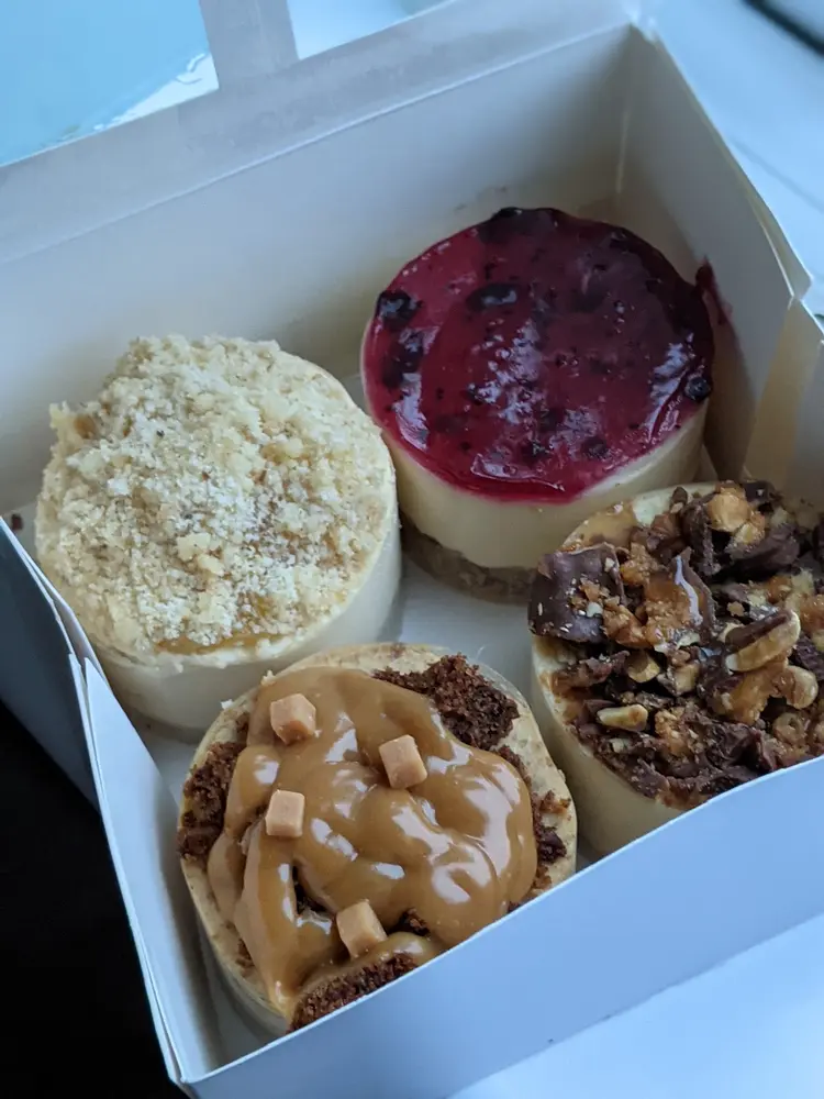 Open box holding five individual cheesecakes with fruit, crumble and chocolate toppings