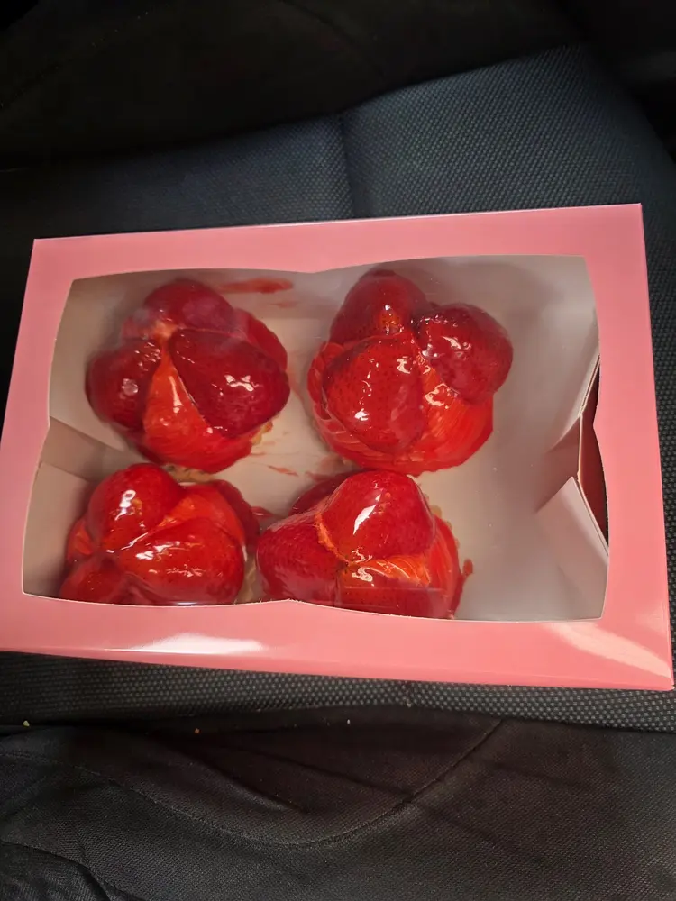 Four strawberry-topped individual cheesecakes in a pink window box