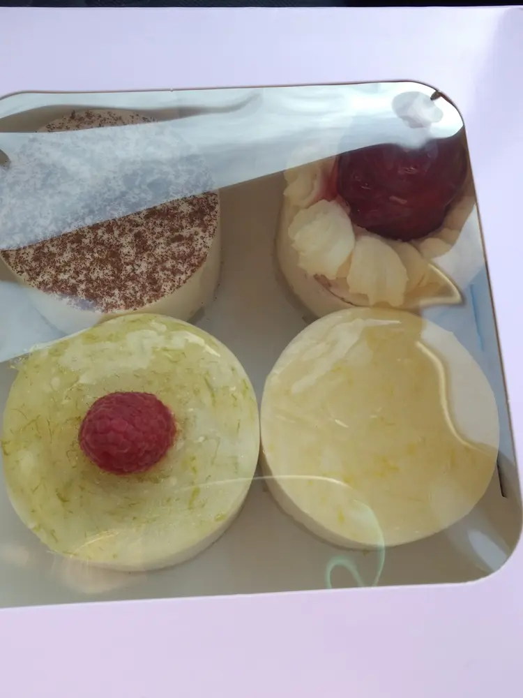 Four individual cheesecakes including lime and raspberry and a cherry-topped one in a white box