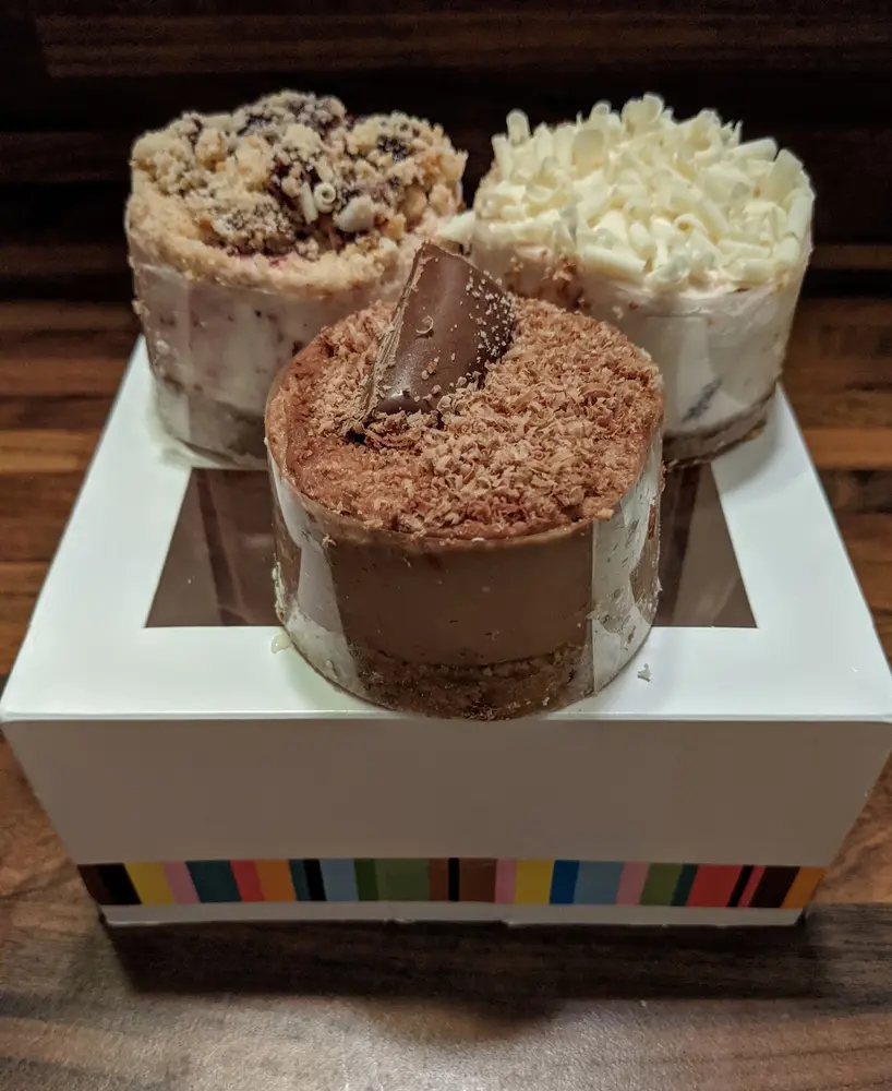 Three individual cheesecakes on a wooden table beside a white bakery box